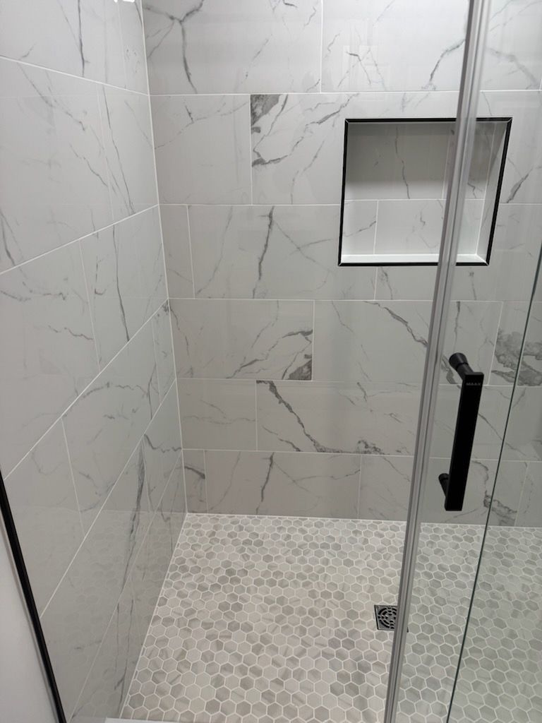 Modern tiled shower with pebble floor, glass door, and recessed niche.