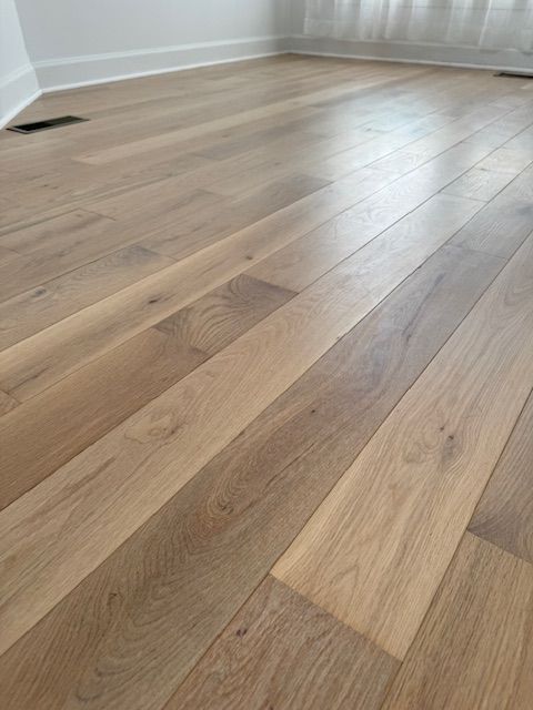 Light oak hardwood floor in an empty room with white walls and baseboards.