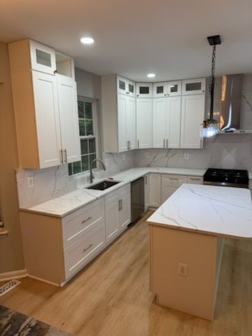 Bright white kitchen with wood floor, marble counters, island, sink, and upper cabinets