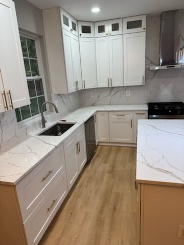 Bright modern kitchen with white cabinets, marble countertops, and light wood flooring