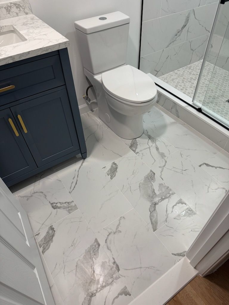 Modern bathroom with white marble tile, a toilet, and a navy vanity by a glass shower door