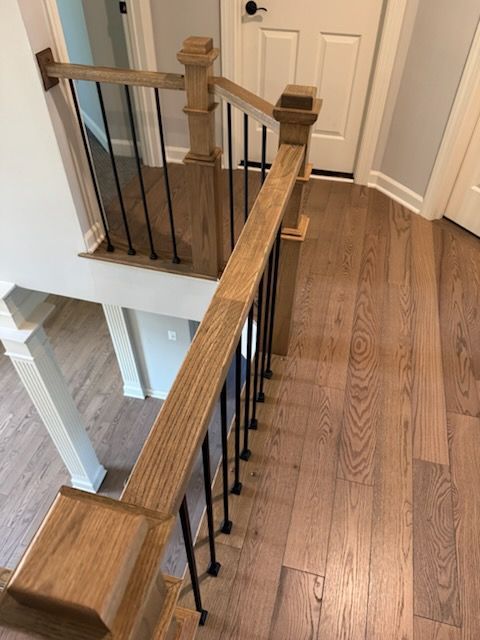 Wooden staircase landing with white railing and black balusters beside a hallway door