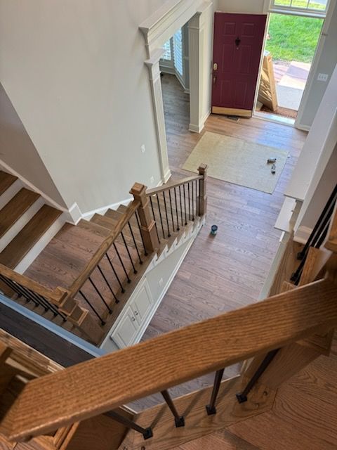 View down a wooden staircase into a bright entryway with front door and foyer floor below