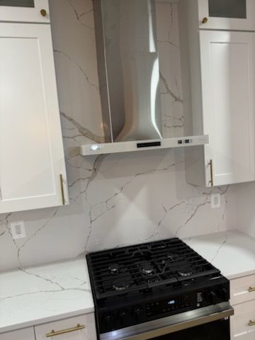 Modern kitchen with white cabinets, marble backsplash, stainless range hood, and black gas stove