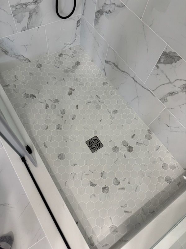 Shower stall with white tiled walls and a pebble-textured floor, featuring a square drain.
