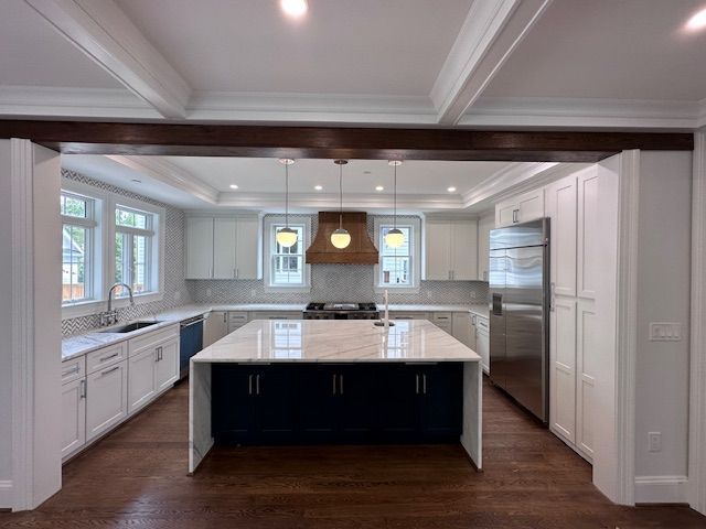Modern kitchen with gray cabinets, stainless steel appliances, white island, and black pendant lights.