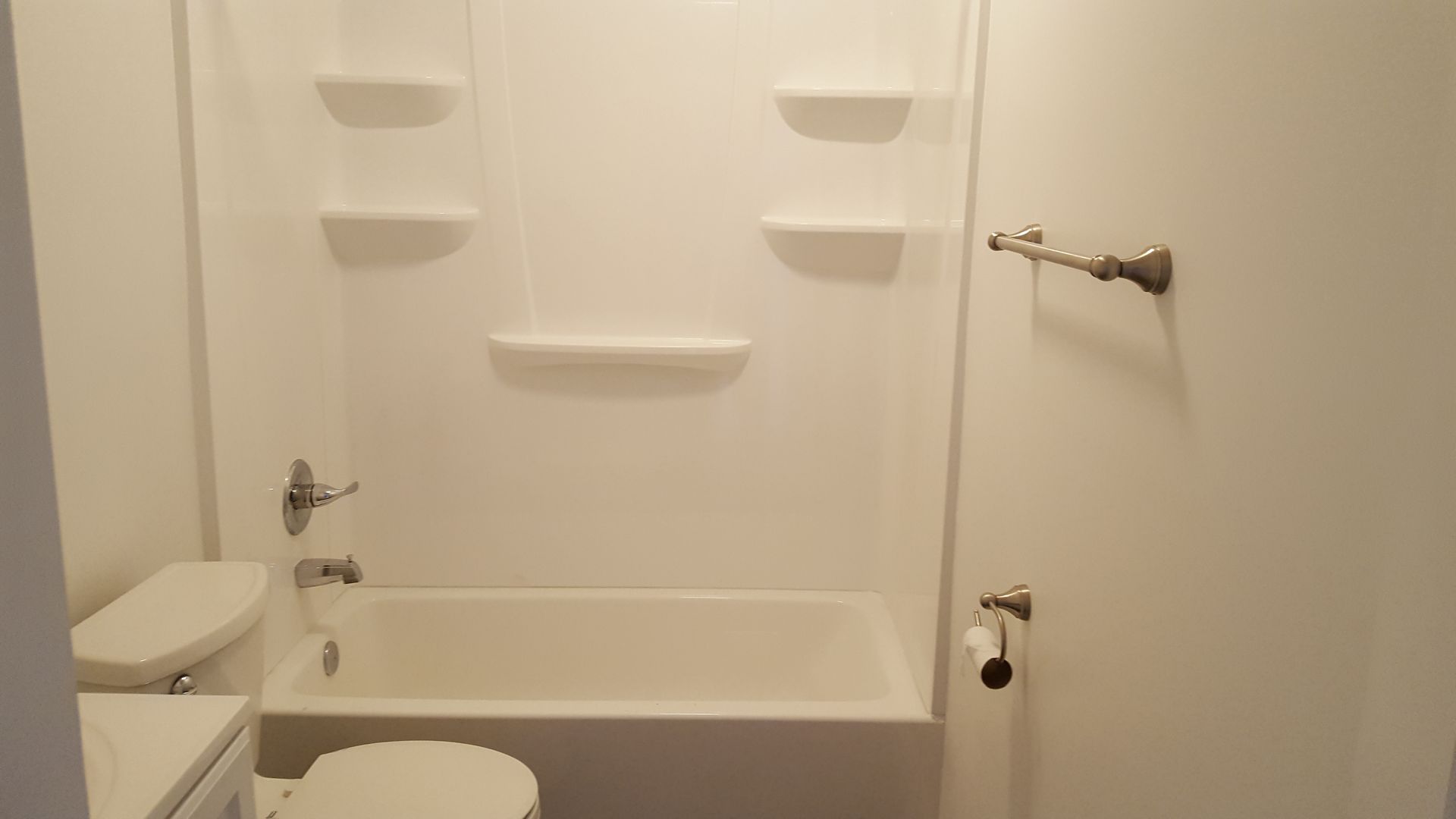 A bathroom with a toilet , tub , shower and shelves.