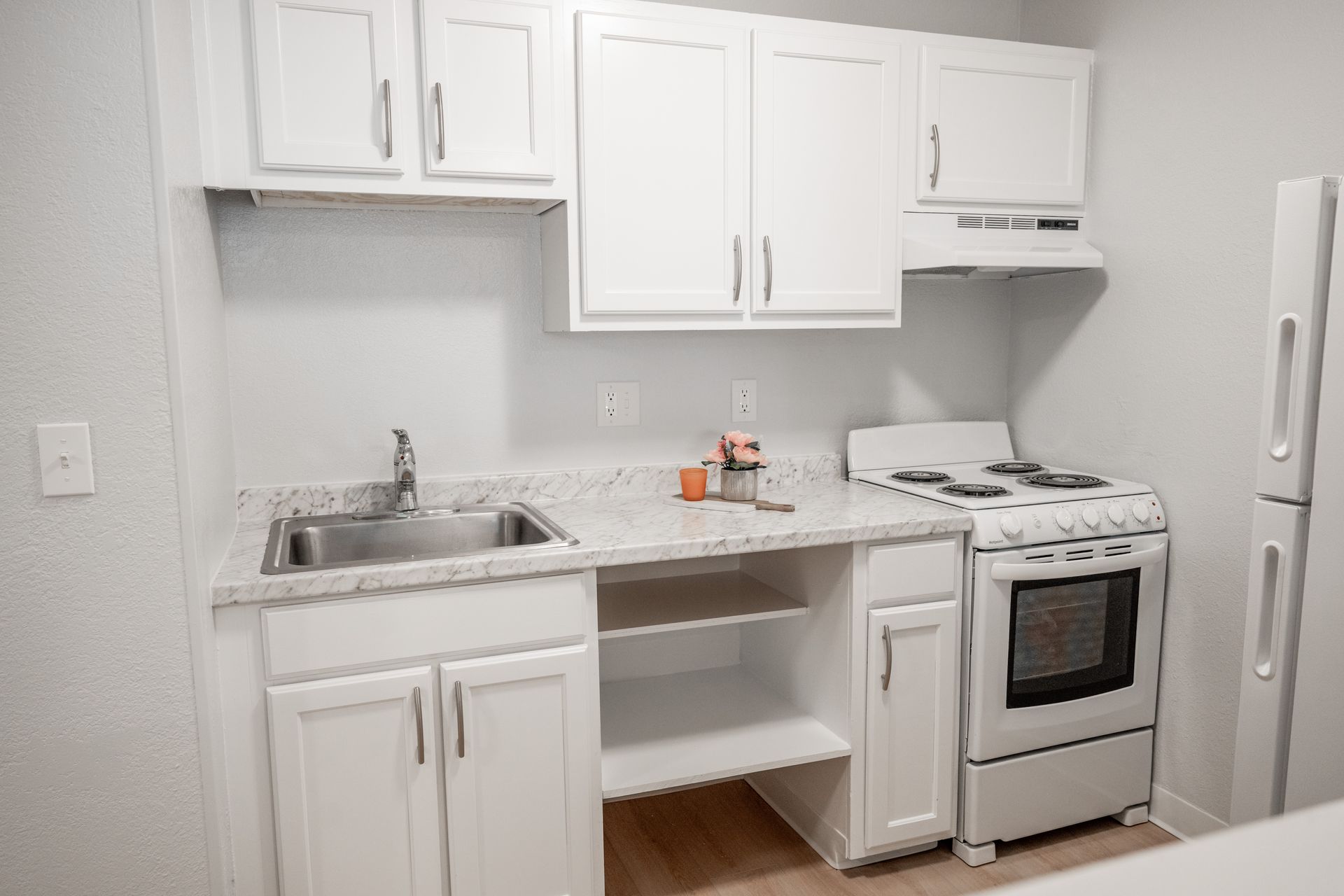 A kitchen with white cabinets , a stove , a sink , and a refrigerator.