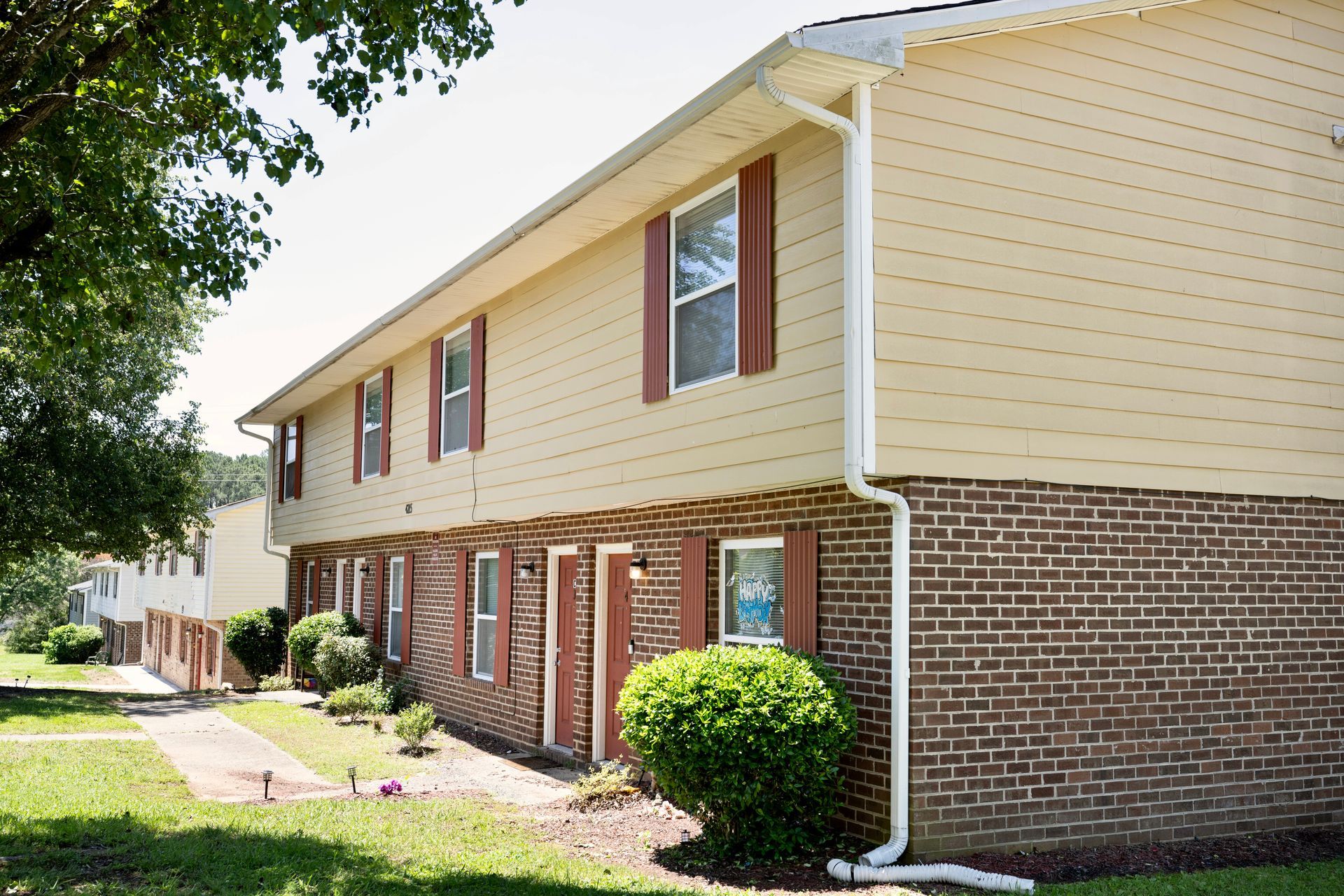 A brick apartment building with a white siding and red shutters