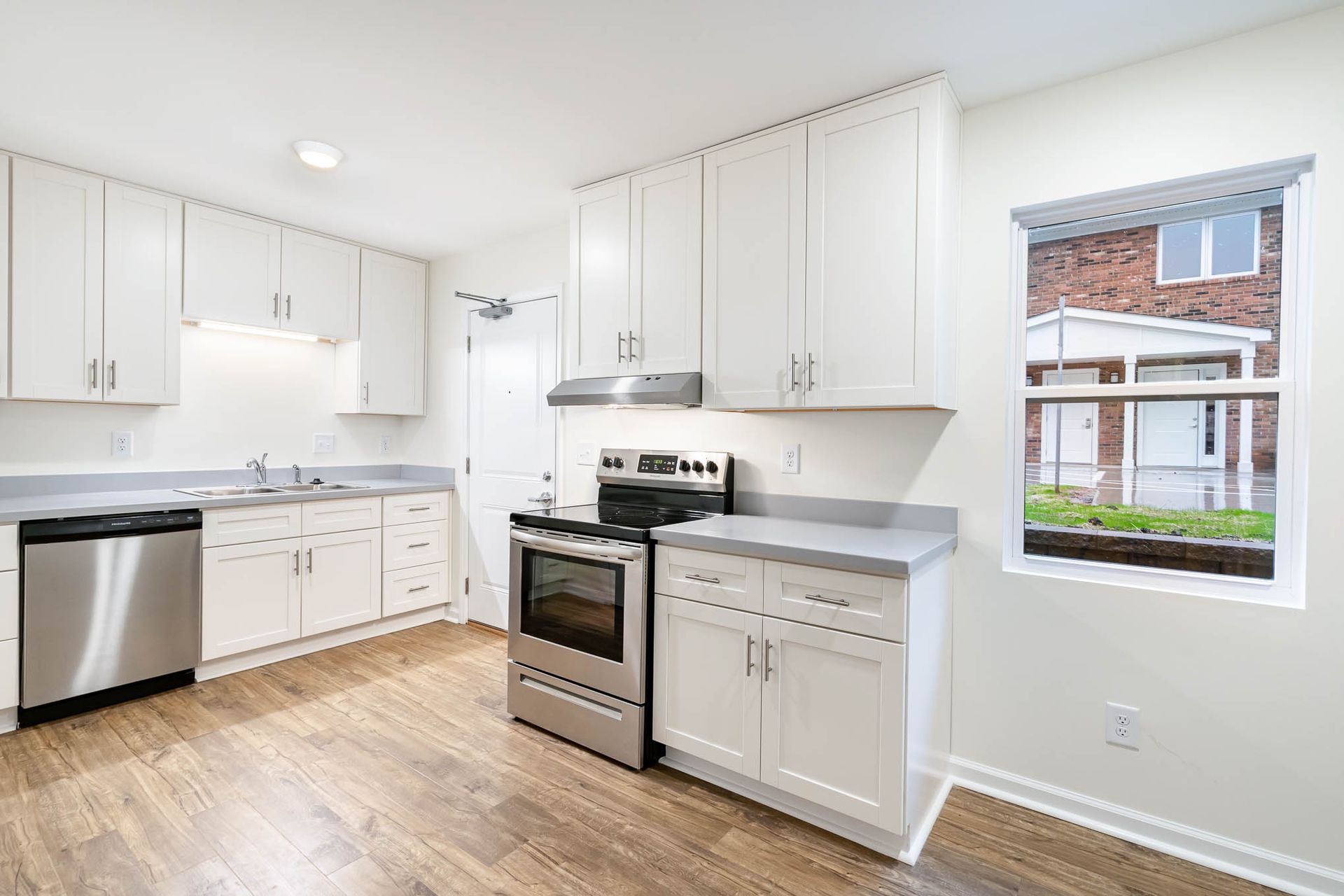 A kitchen with white cabinets , a stove , a dishwasher , and a window.
