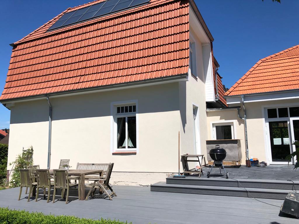 Ein weißes Haus mit einem roten Ziegeldach hat eine Terrasse mit Tisch und Stühlen