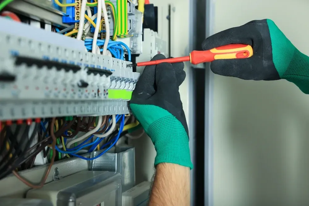 An electrician wearing gloves uses a screwdriver on a circuit breaker panel. — Brian Williams Electrical Air Solar in Cooroibah, QLD