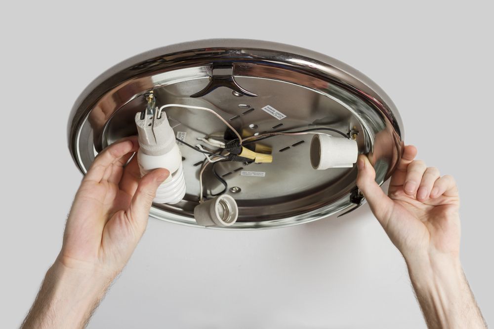 Hands Installing a Lightbulb Into a Ceiling Light Fixture — Brian Williams Electrical Air Solar in Caloundra, QLD