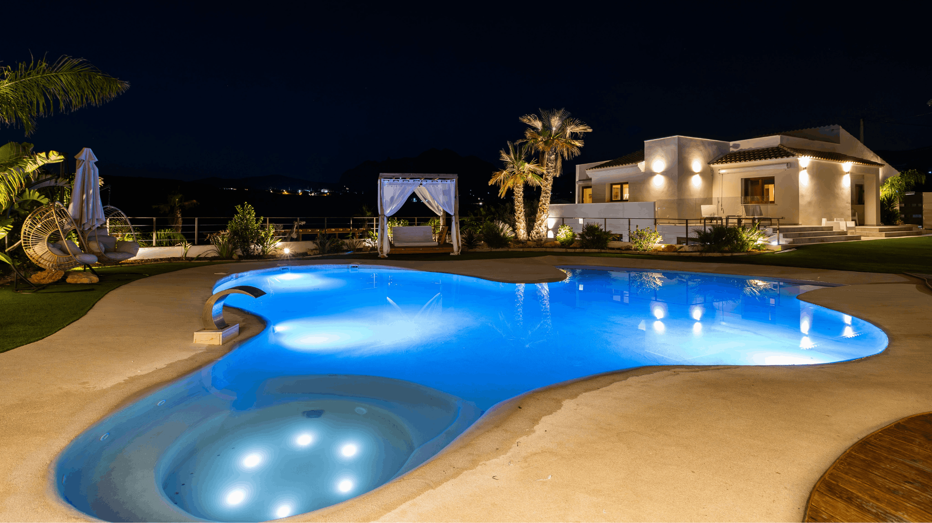 Nighttime view of a blue, illuminated pool in front of a white house — Brian Williams Electrical Air Solar in Cooroibah, QLD