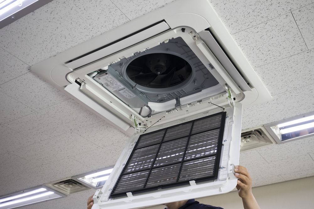 A Person Opens the Hinged Front Panel of a Ceiling-mounted Hvac Unit — Brian Williams Electrical Air Solar in Cooroibah, QLD