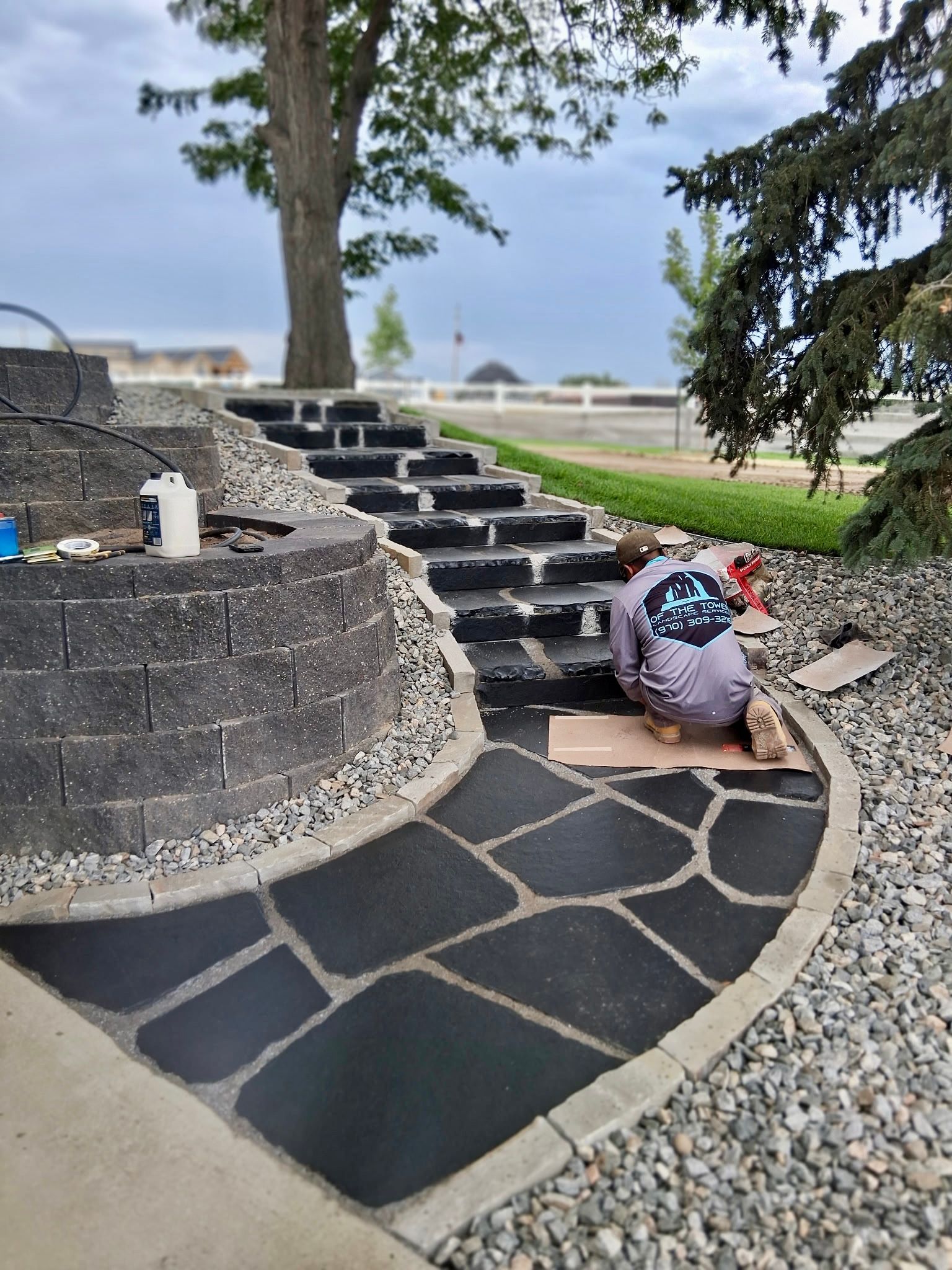 Stone path leads past a rock garden, fire pit, and fence in a backyard.