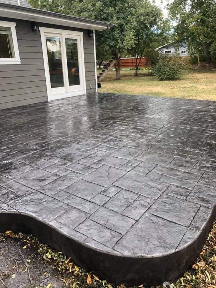 Dark gray stamped concrete patio with curved border, next to a house with French doors.