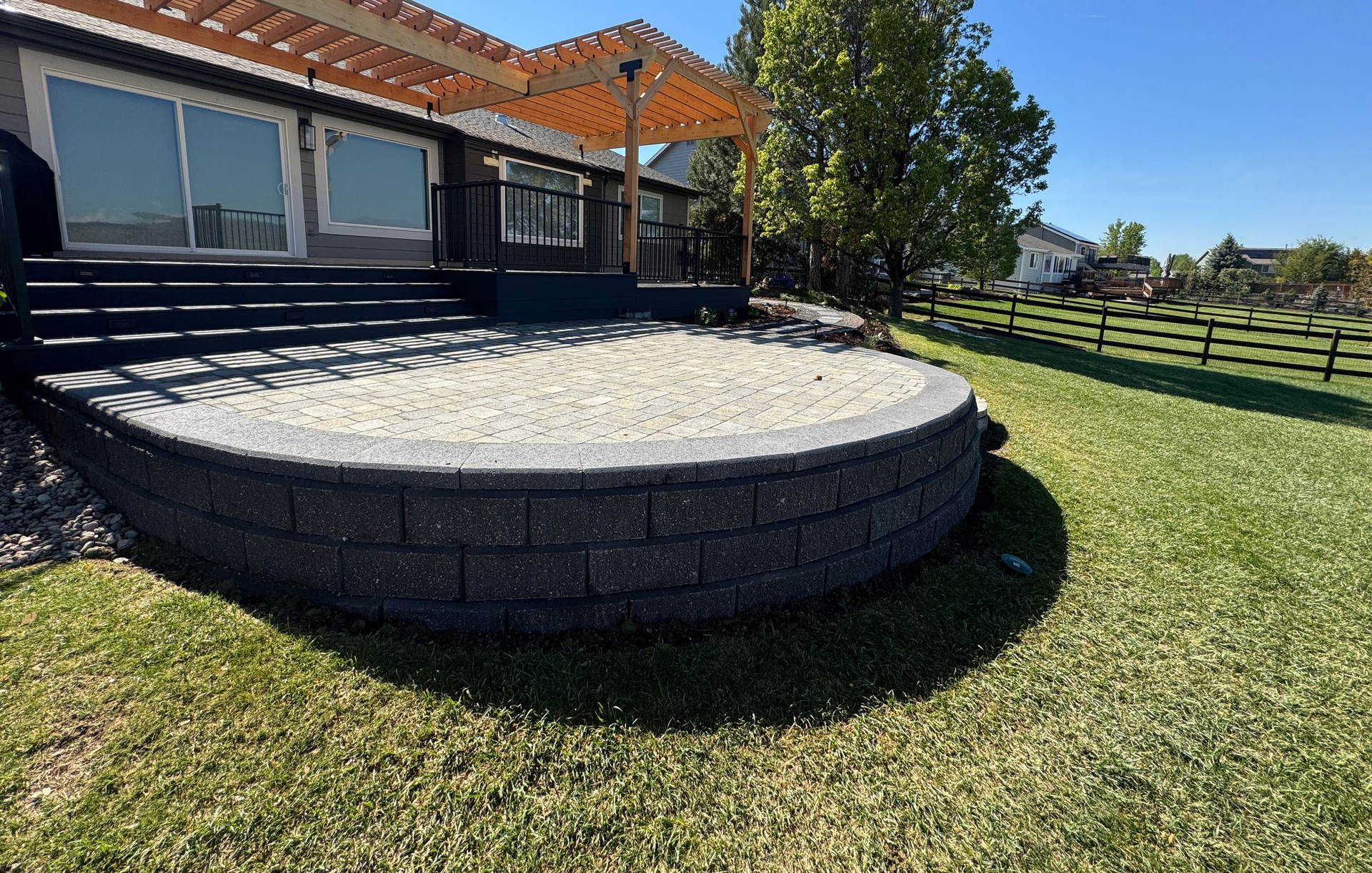 House patio with a round stone raised bed and green lawn under a sunny sky