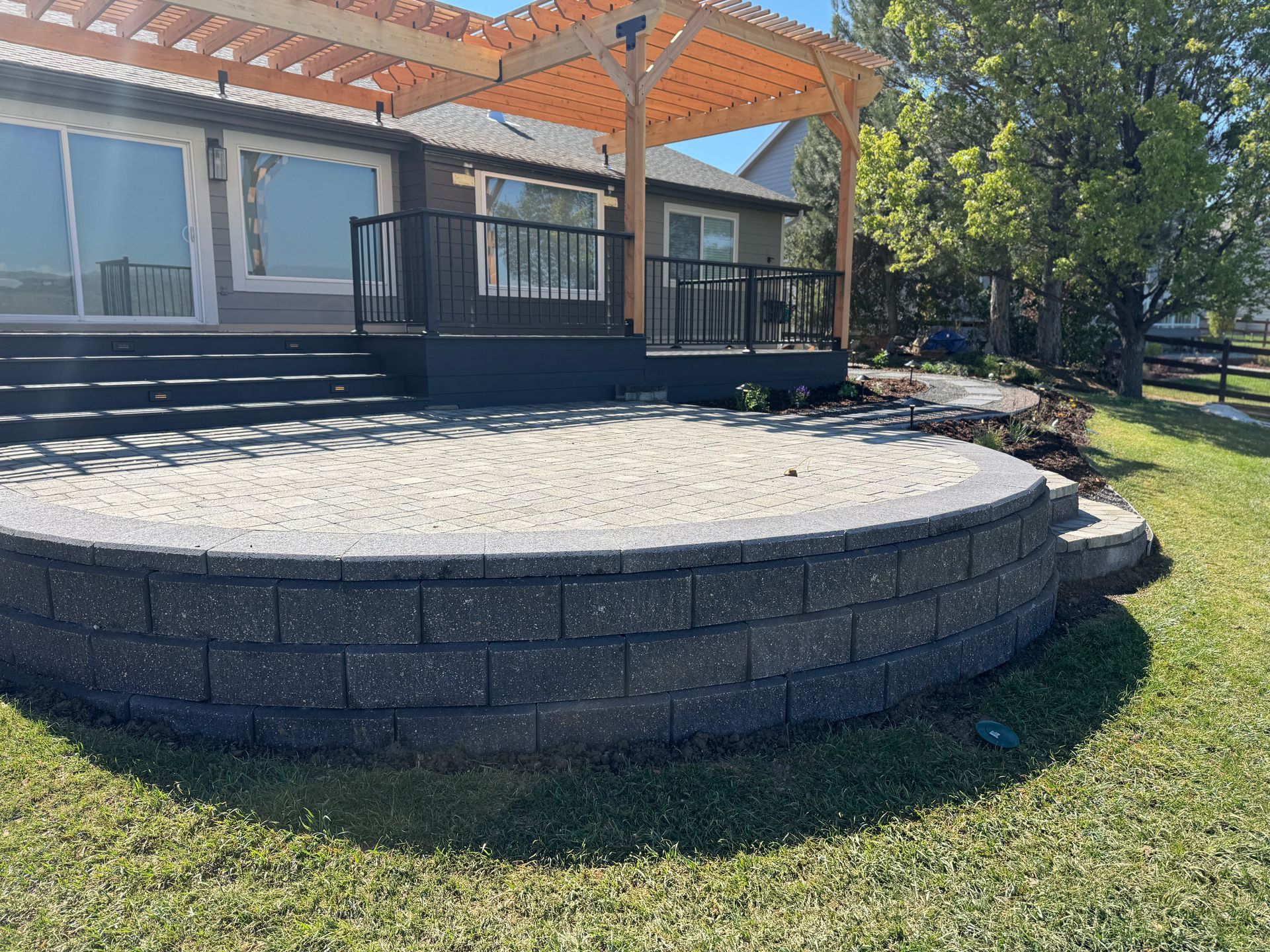 A patio with a retaining wall next to a deck with a pergola in a yard.