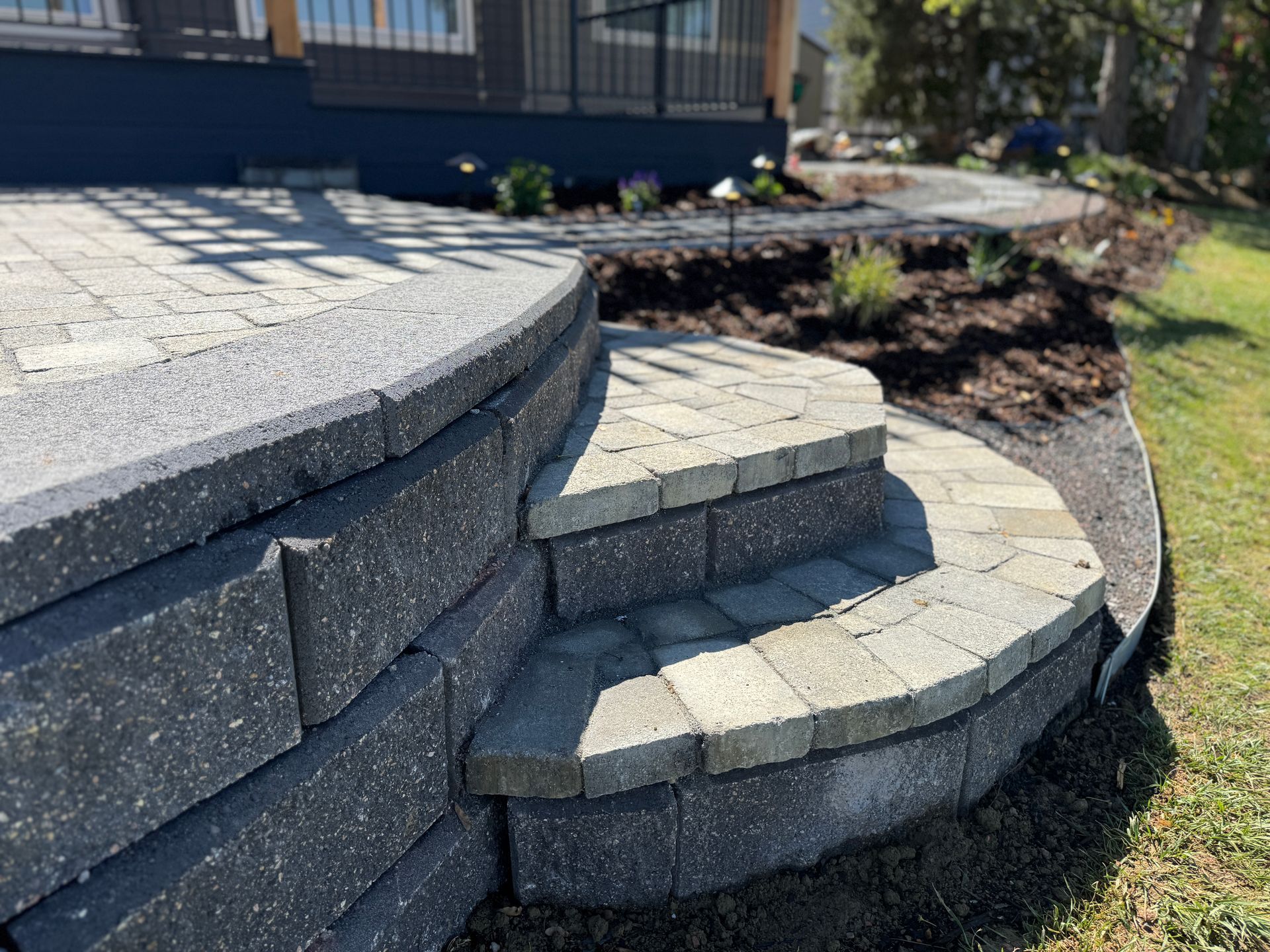 Stone steps in a park beside a stone wall, with people sitting at the top near a playground and grassy slope.
