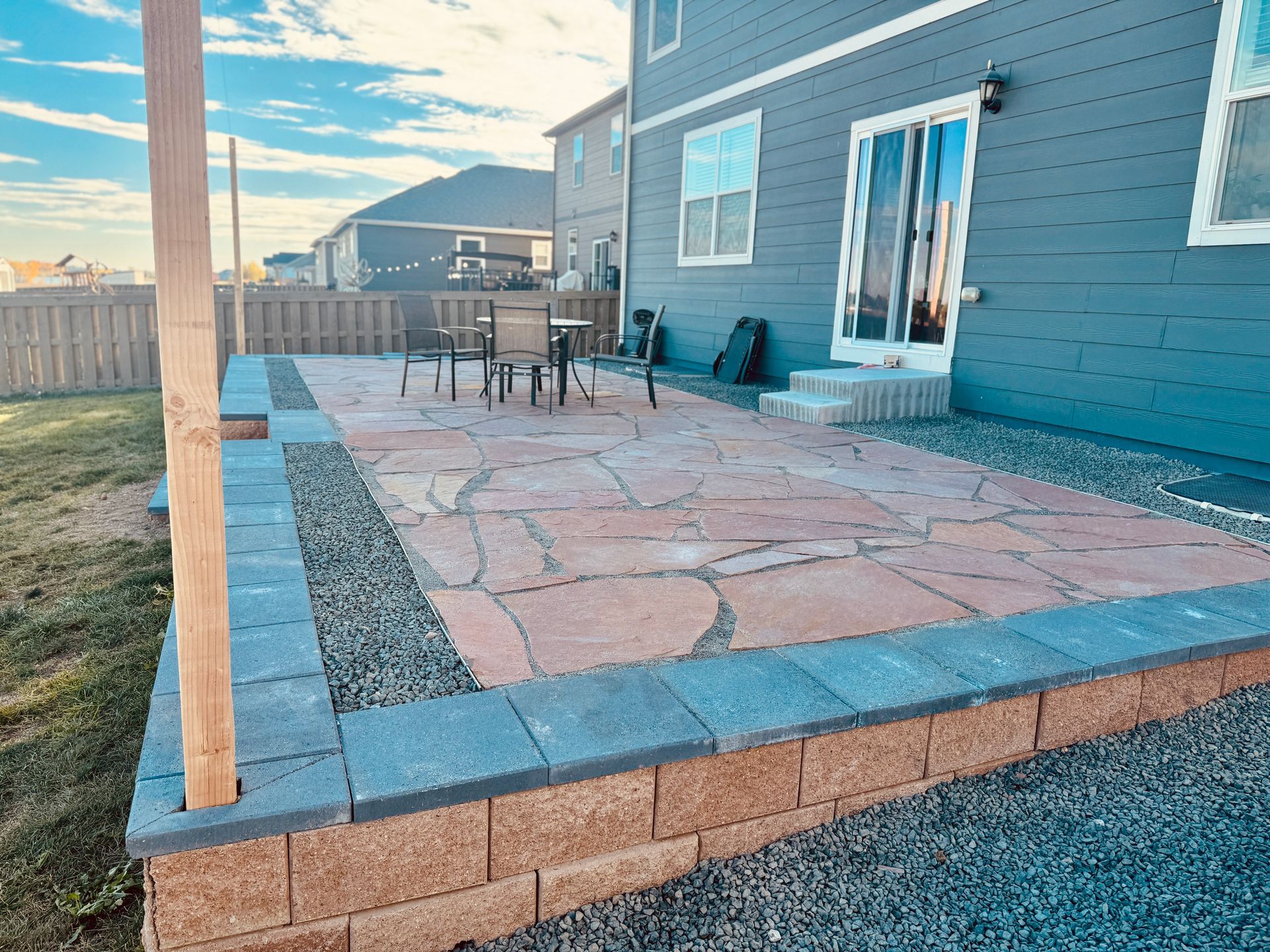 Stone path leads past a rock garden, fire pit, and fence in a backyard.