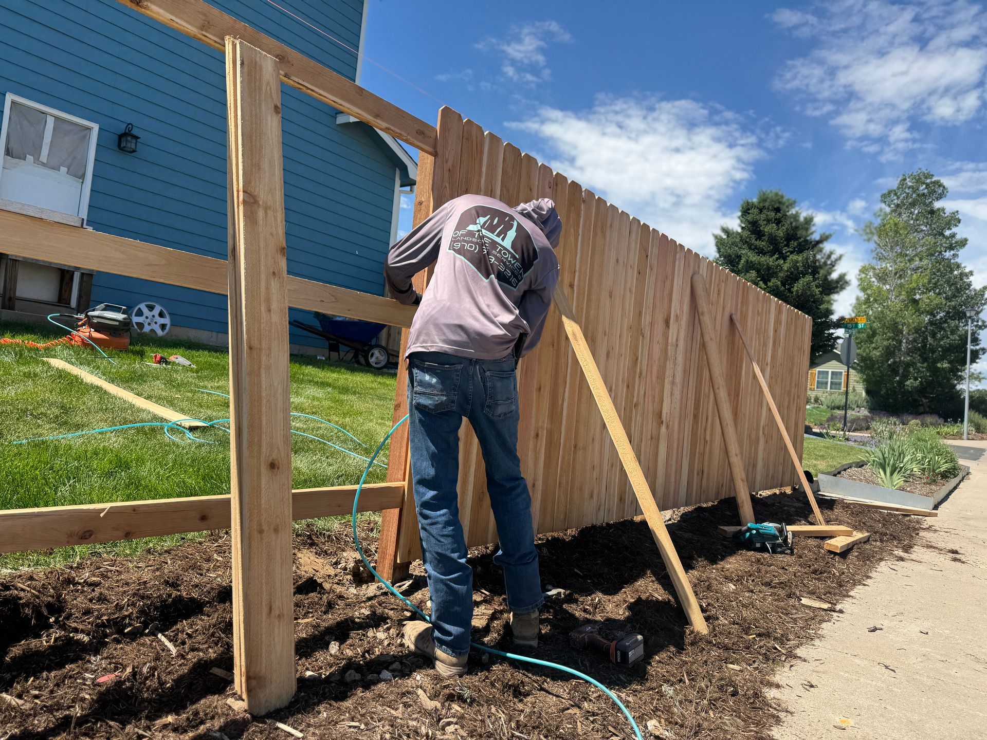 A person builds a fence on a grassy lawn with wooden posts and rails, sunny day.