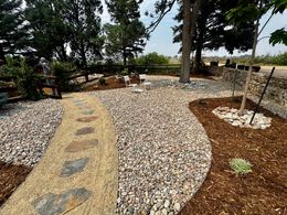 Gravel garden path with stone steps, mulch beds, and trees in a landscaped yard