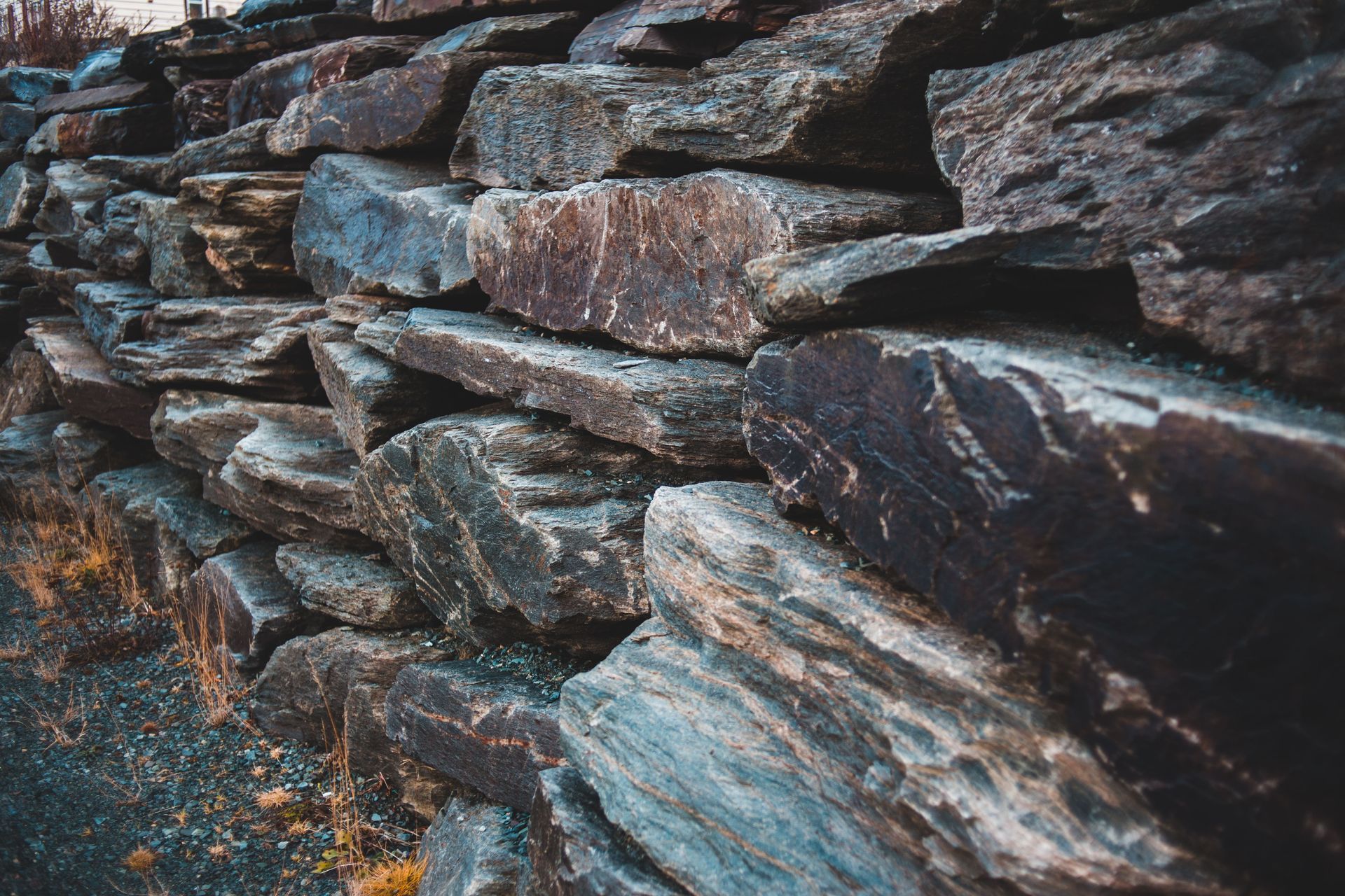 Stacked dark stone wall with rough, layered rocks in blue-gray and brown tones