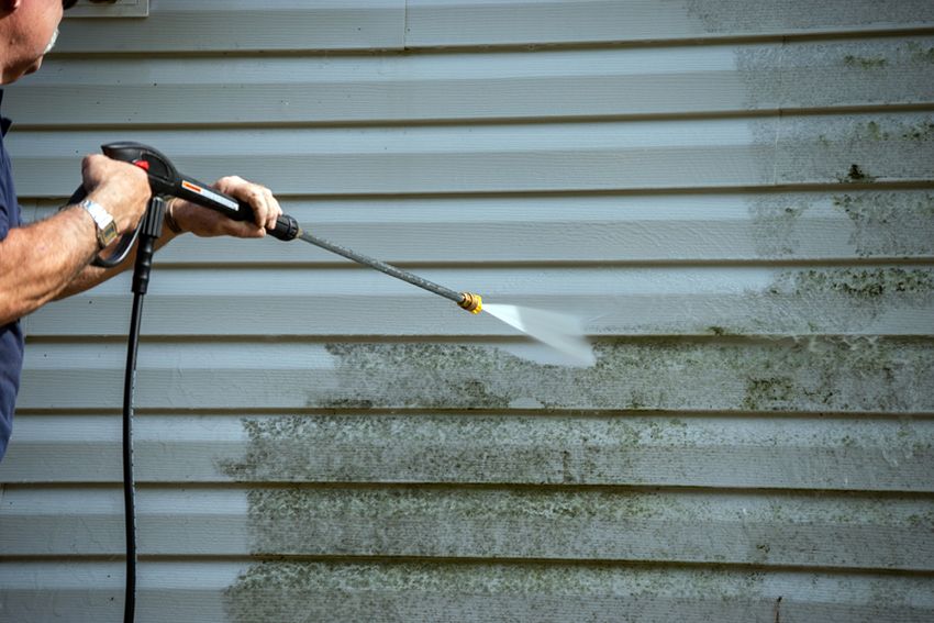 A Man is Cleaning the Side of a House with a High Pressure Washer — Painters Geelong in Geelong, VIC