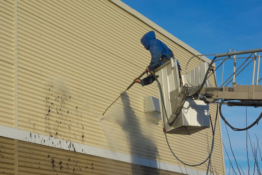 A Man is Cleaning a Building with a High Pressure Washer — Painters Geelong in Geelong, VIC