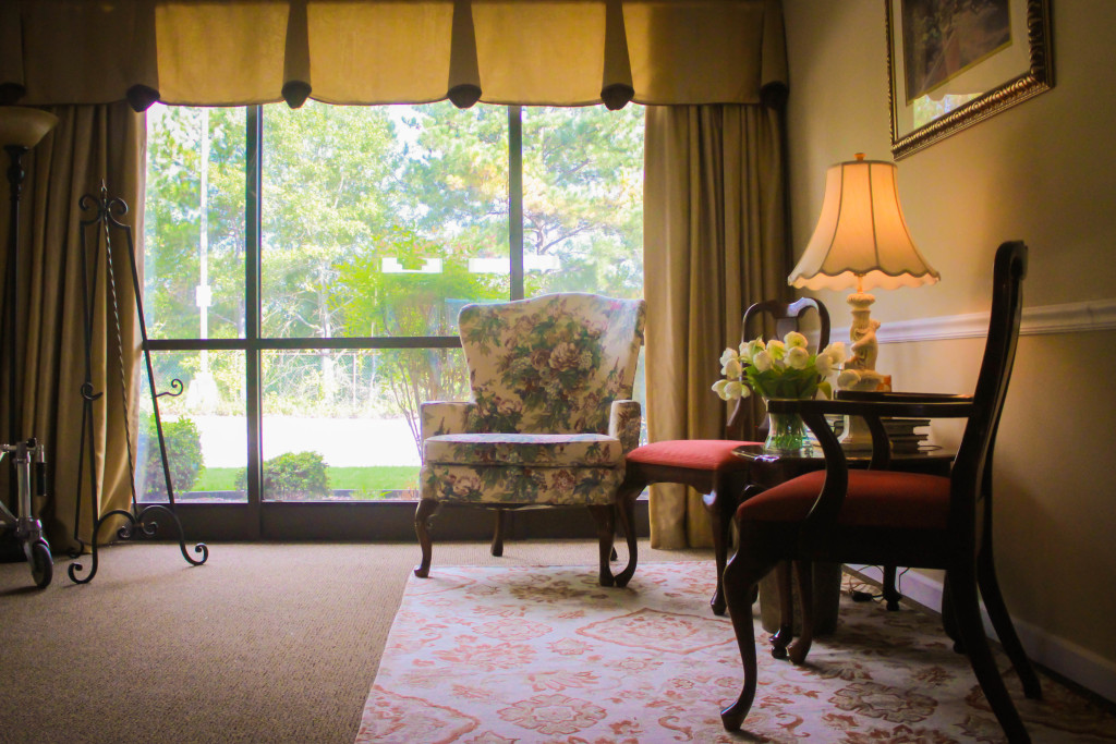 Cozy living room with large window, armchairs, lamp, and a table on a patterned rug