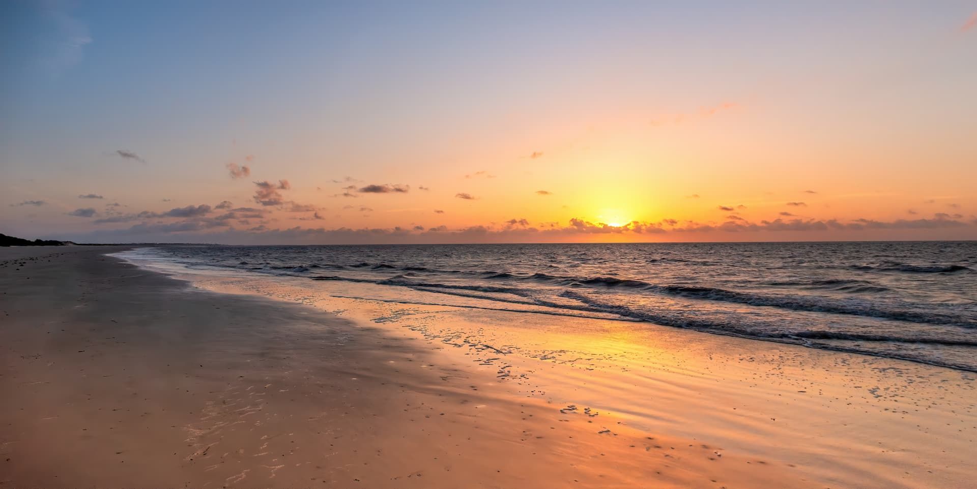 Sunset over a calm beach with golden reflections on the wet sand and gentle waves