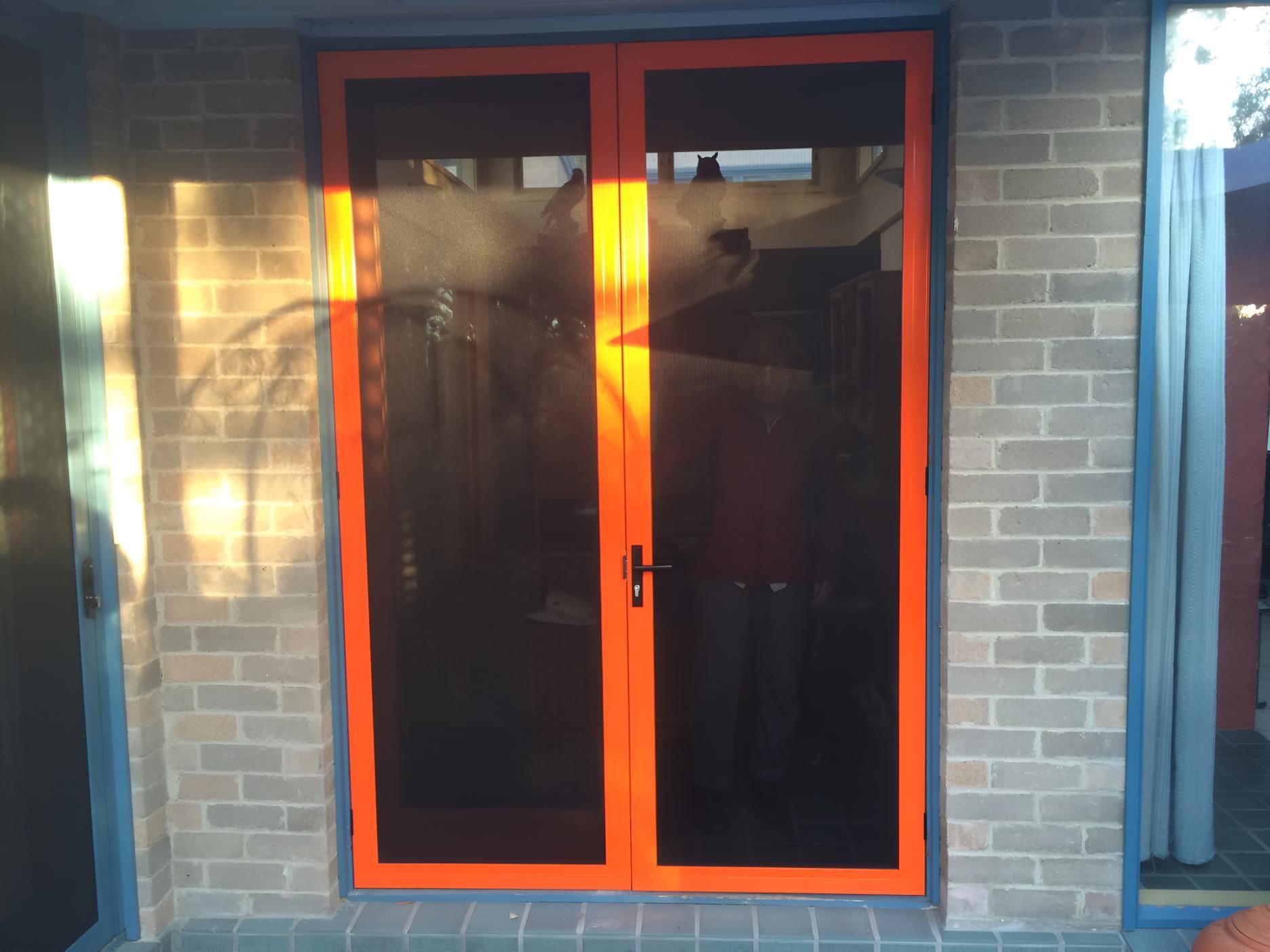 A Pair of Orange Sliding Glass Doors on a Brick Wall — Clearshield Security Screens in Wollongong, NSW