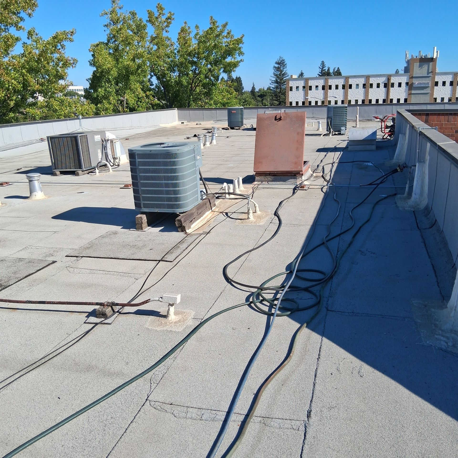 Rooftop with HVAC units, cables, and low parapet walls under a clear blue sky