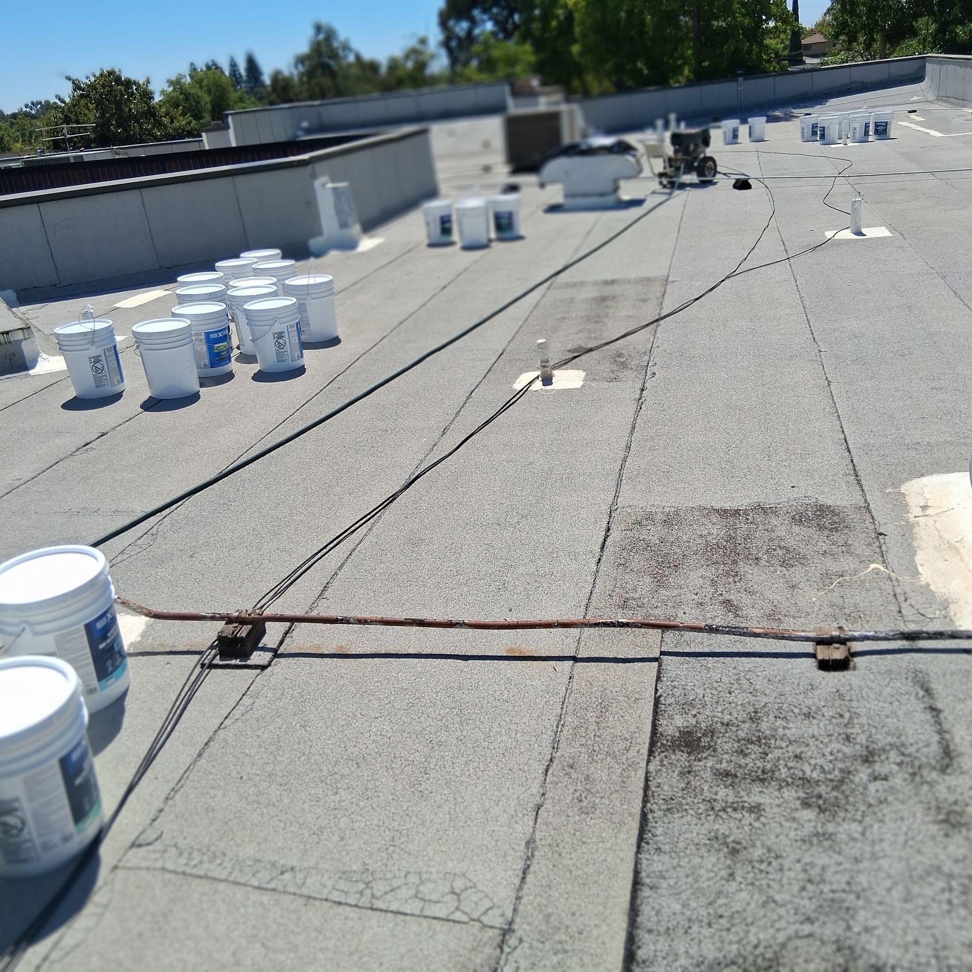 Rooftop with white buckets, gravel surface, and visible cables in bright sunlight.