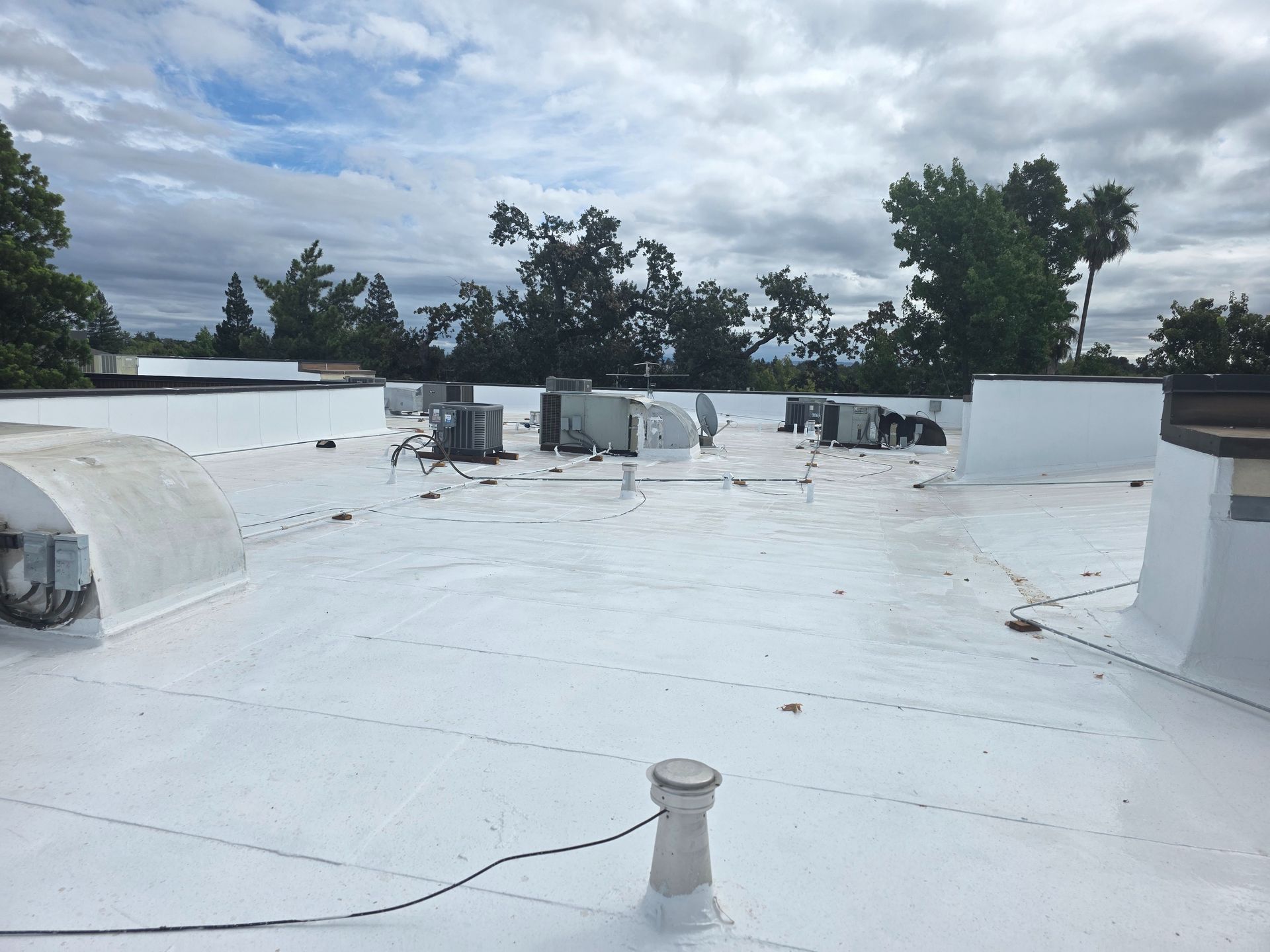 White flat rooftop with vents and HVAC units under a cloudy sky.