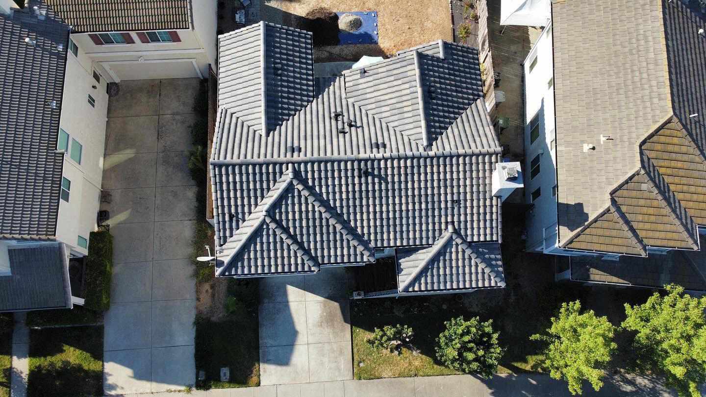Aerial view of a gray-tiled house roof with neighboring homes and trees around it