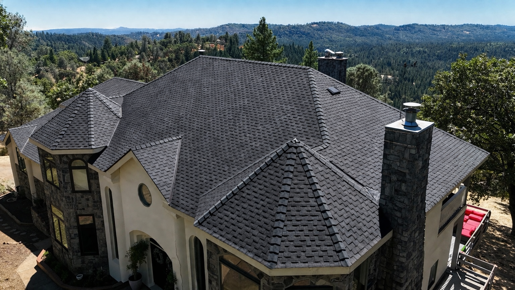 A large stone house with a dark shingled roof overlooking a wooded valley and distant hills