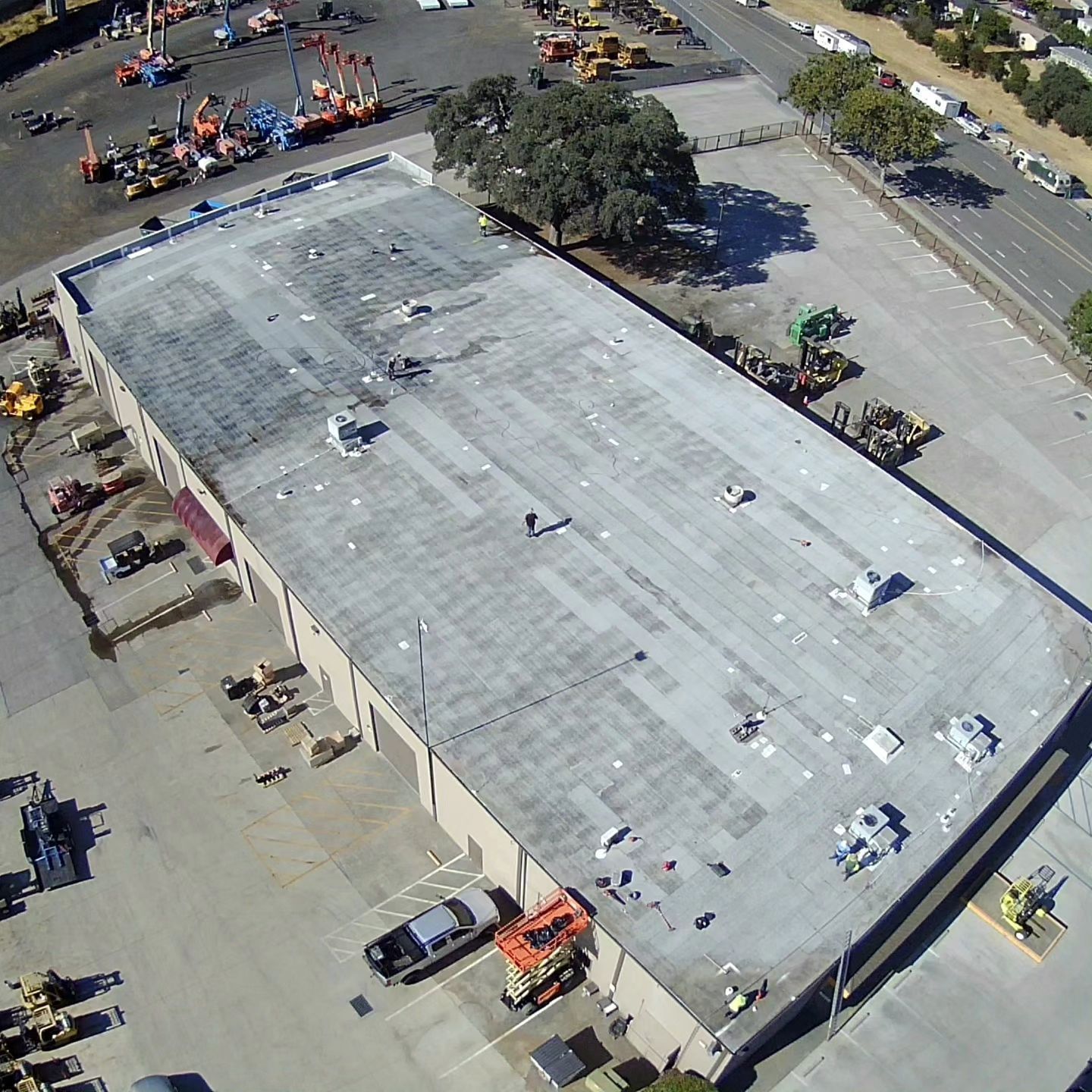 Aerial view of a large flat-roofed building with construction equipment and workers around it.