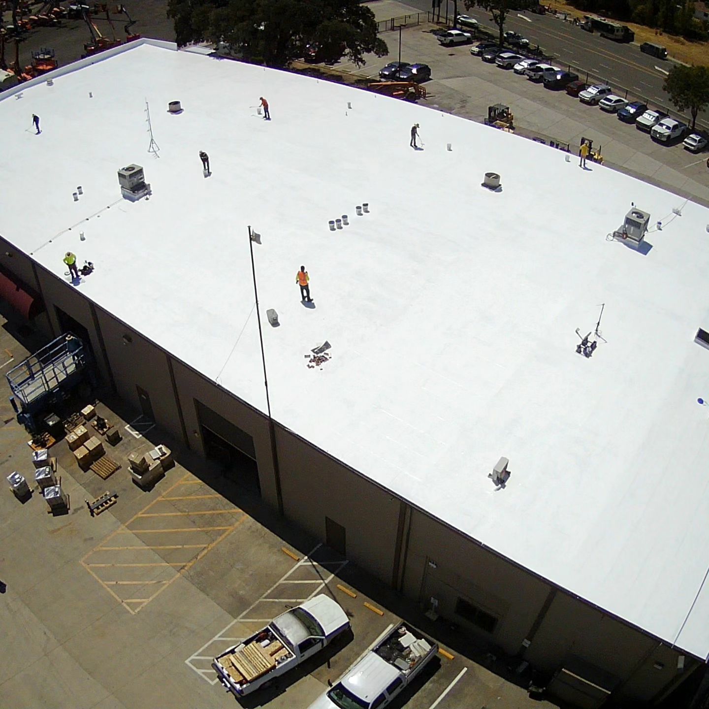 Aerial view of a large white warehouse roof with HVAC units and a parking lot below.
