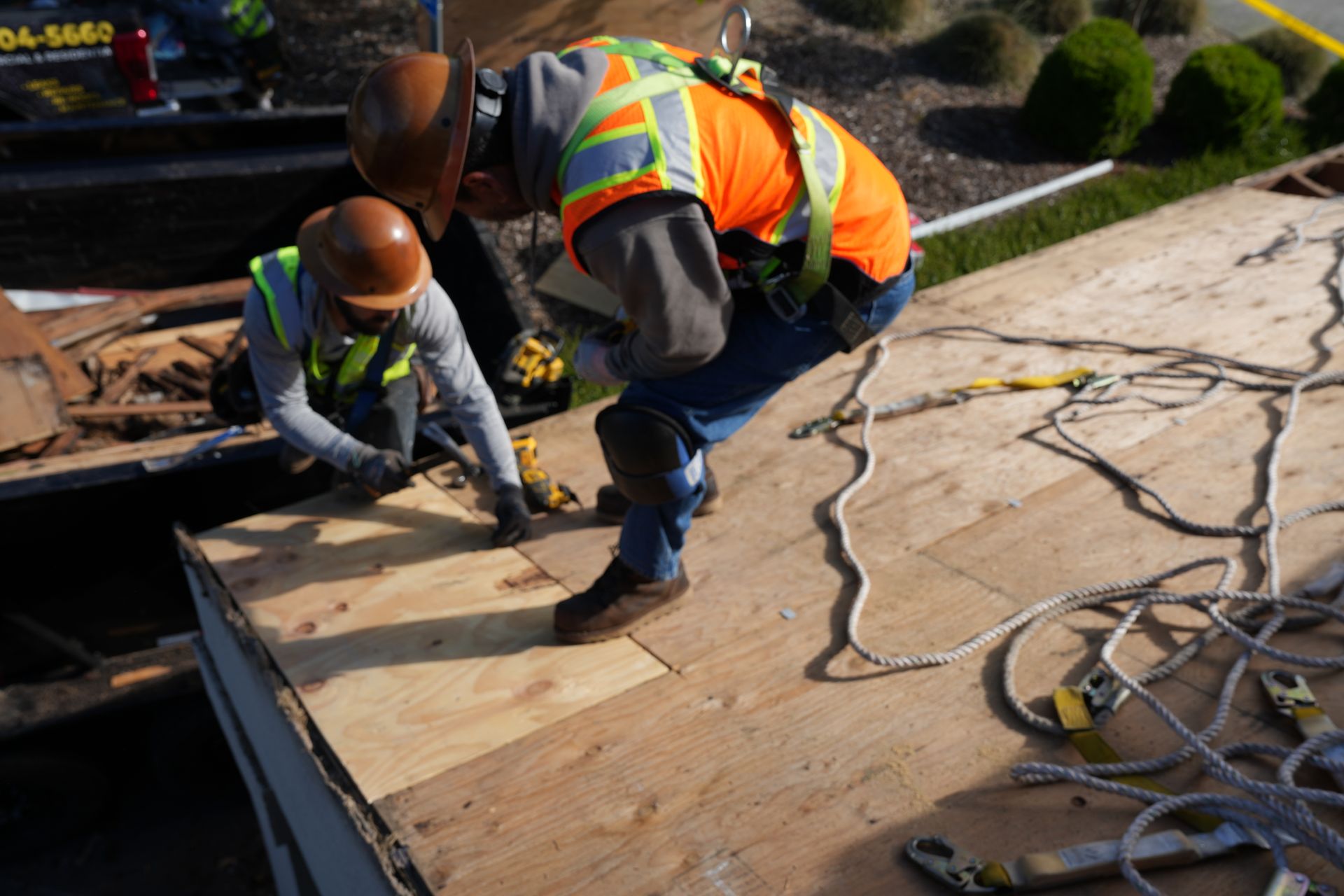Workers in orange safety vests repairing a roof with power tools and lumber