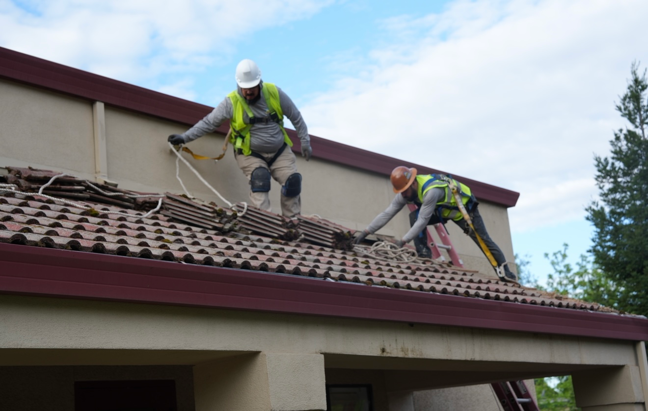 Two workers in safety gear fixing a red-tiled roof on a house