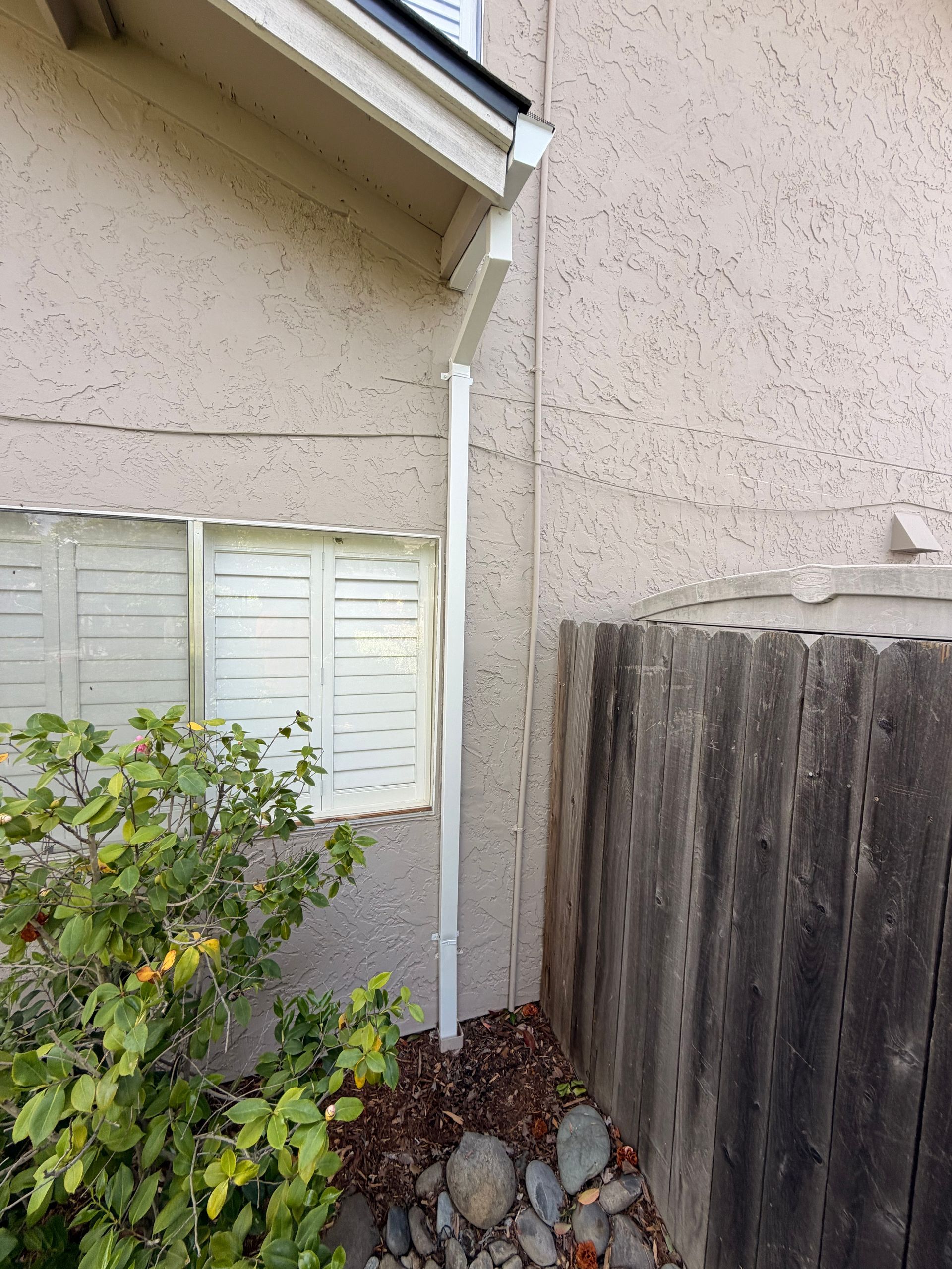 White gutter downspout dripping water from a roof edge indoors, with a wooden ceiling and wall below