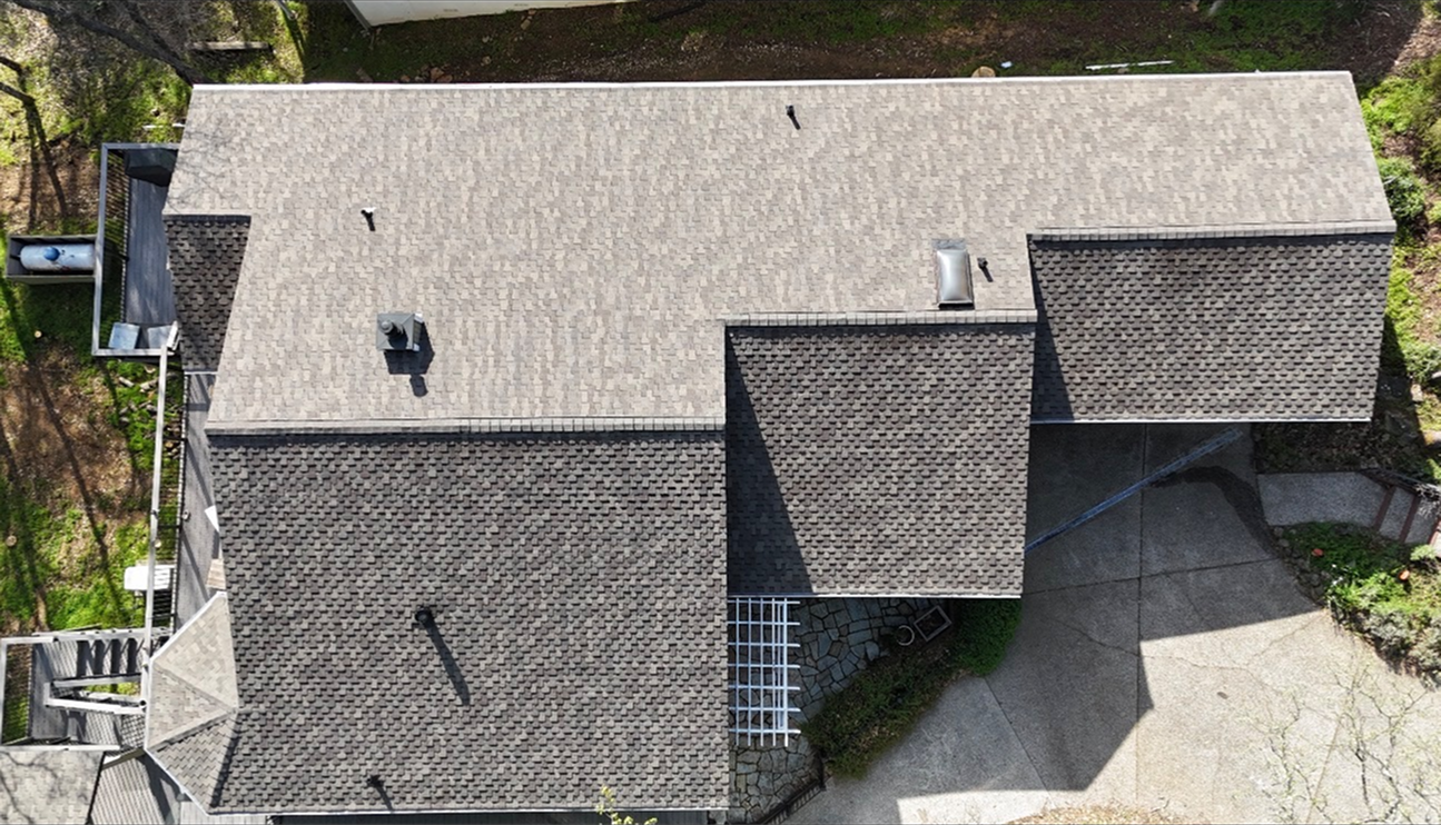 Aerial view of a gray shingled house roof with multiple sections and a small driveway