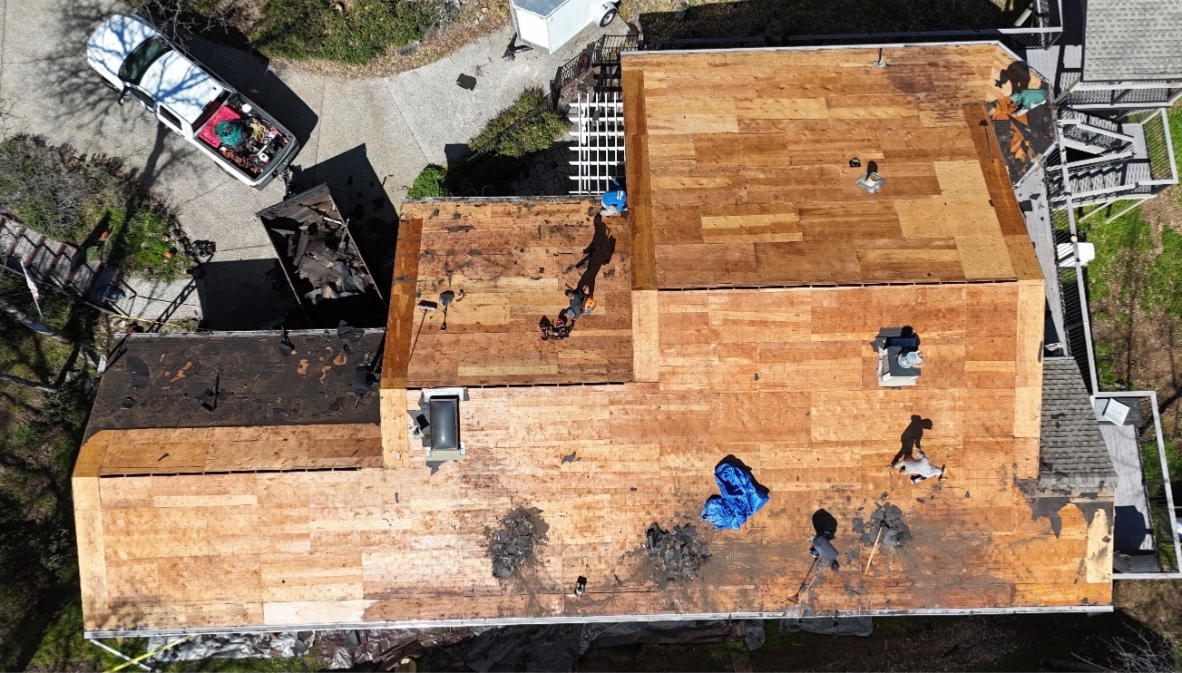 Aerial view of a house roof with several workers doing repairs and a ladder nearby