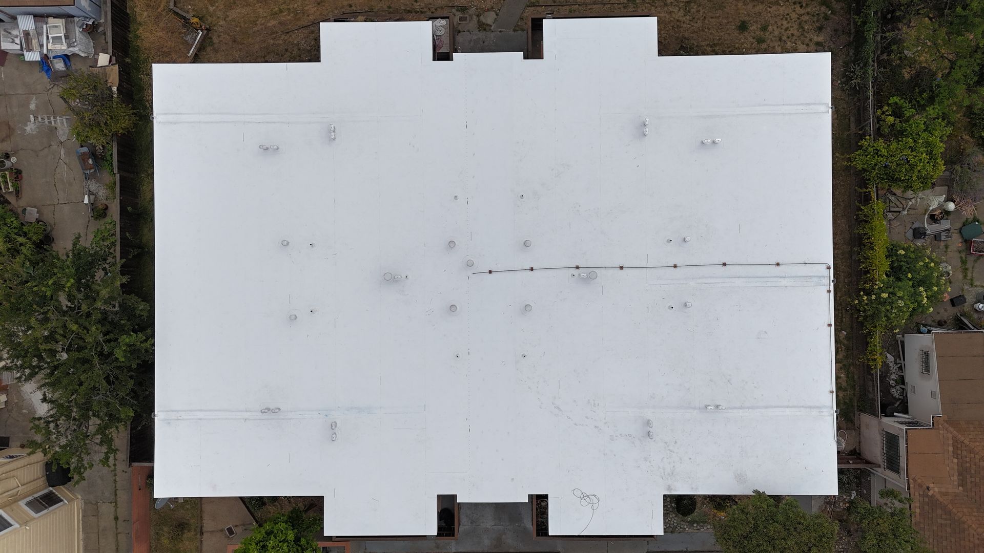 Aerial view of a white flat-roofed building surrounded by trees and neighboring houses.