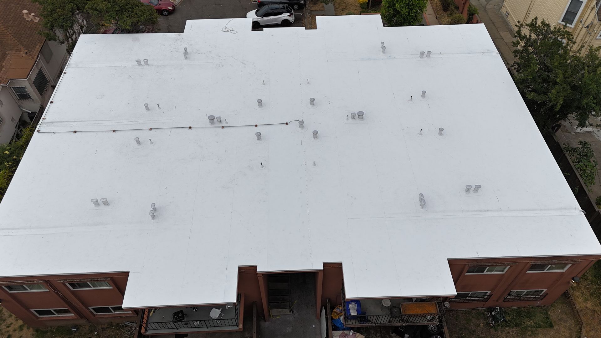 Aerial view of a large building with a flat white roof, brick walls, and trees around it.