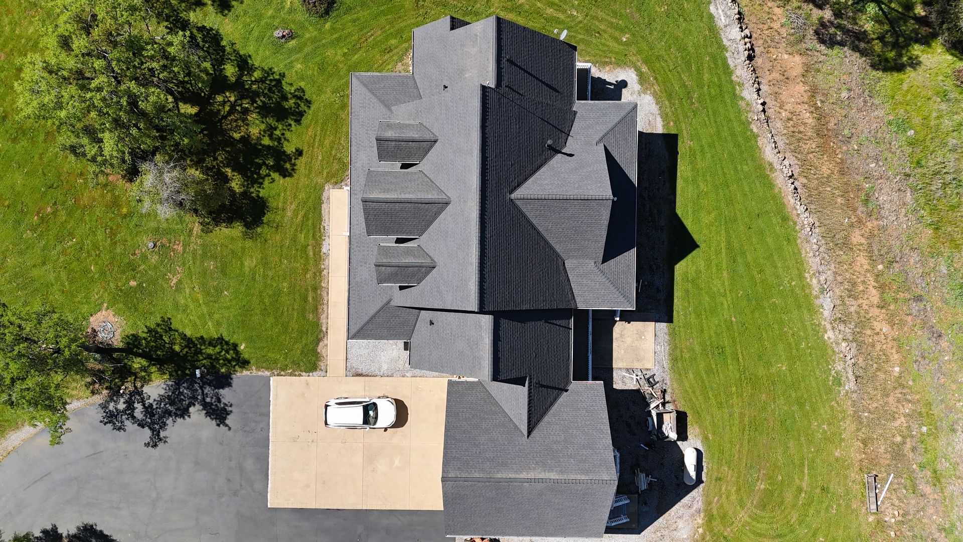 Aerial view of a gray-roofed house with a white car parked on the driveway next to green lawns.