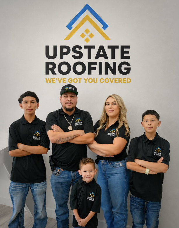 Upstate Roofing team posing in branded black shirts beneath company logo and slogan on a gray wall