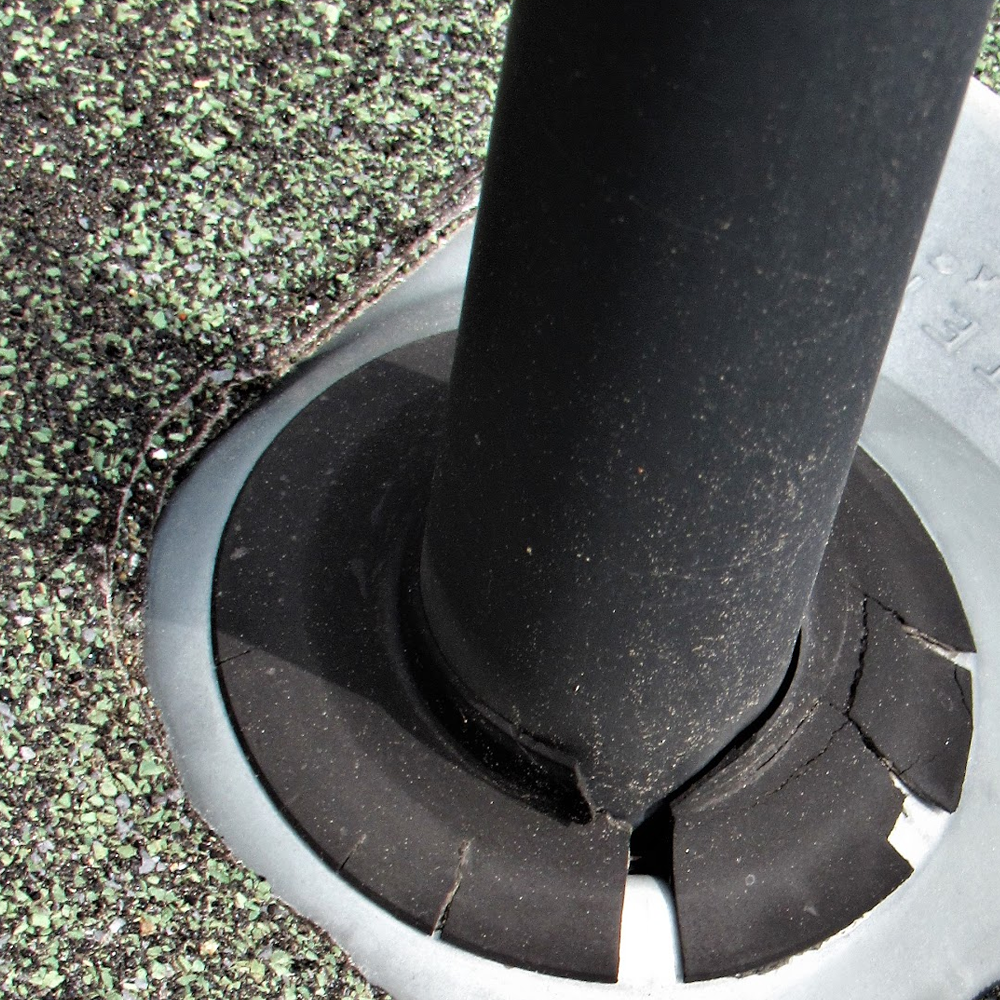 Black pole in a cracked circular base on a rough outdoor surface.